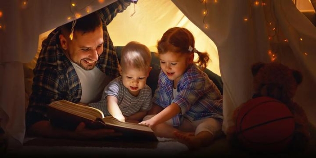 Man and two kids in a tent looking at a book